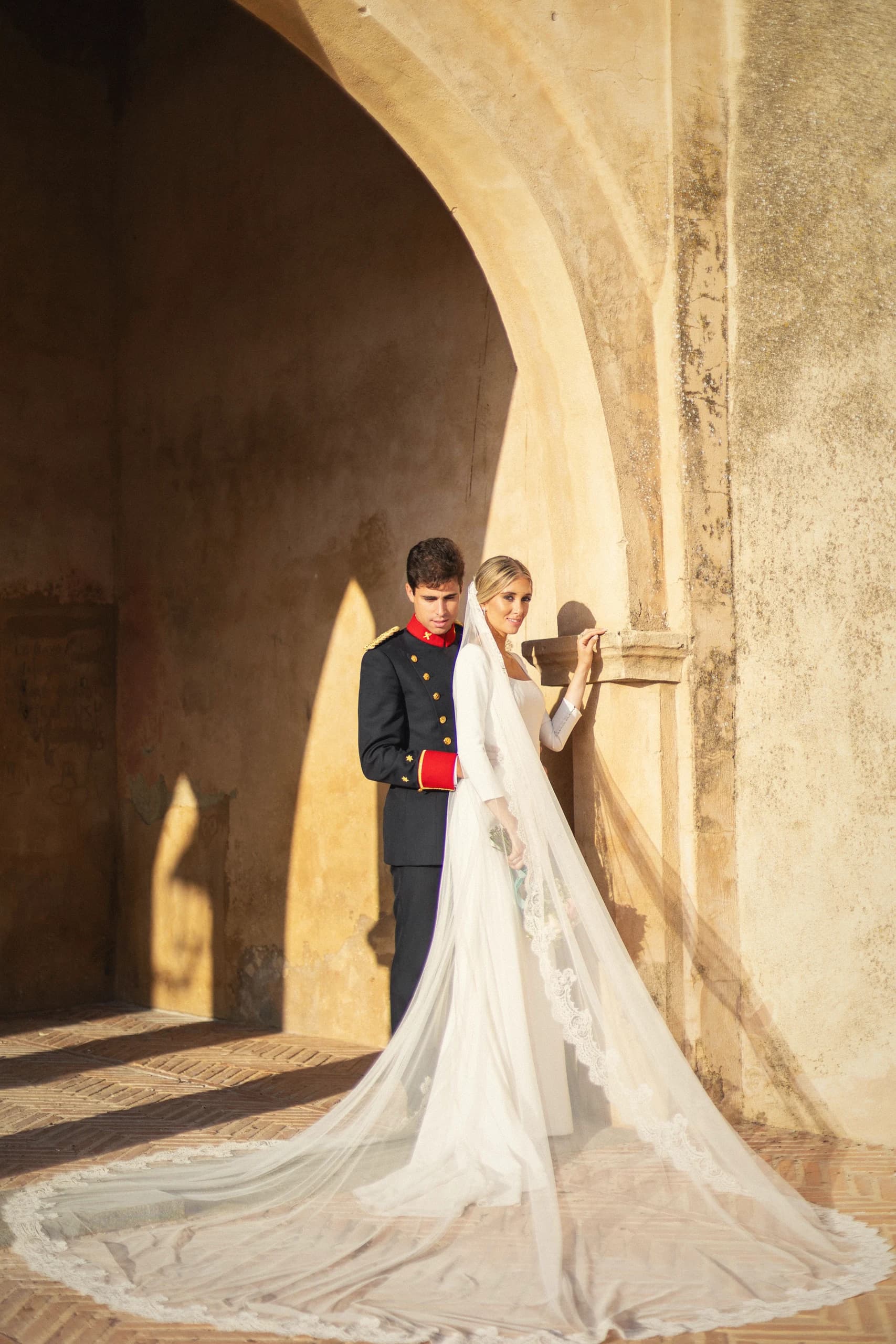 La novia y el novio bajo el arco de piedra con la cola extendida