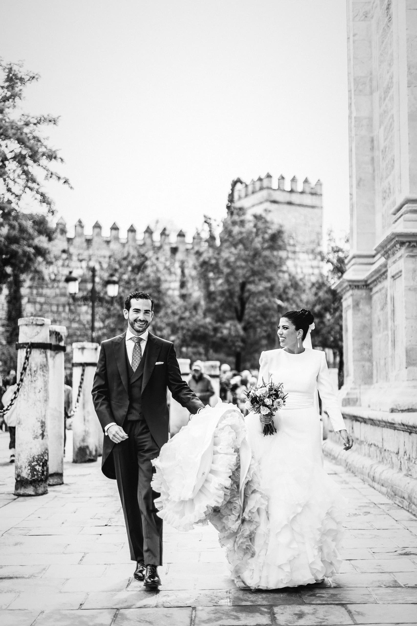 Los novios caminando de la mano bajo la muralla, en blanco y negro