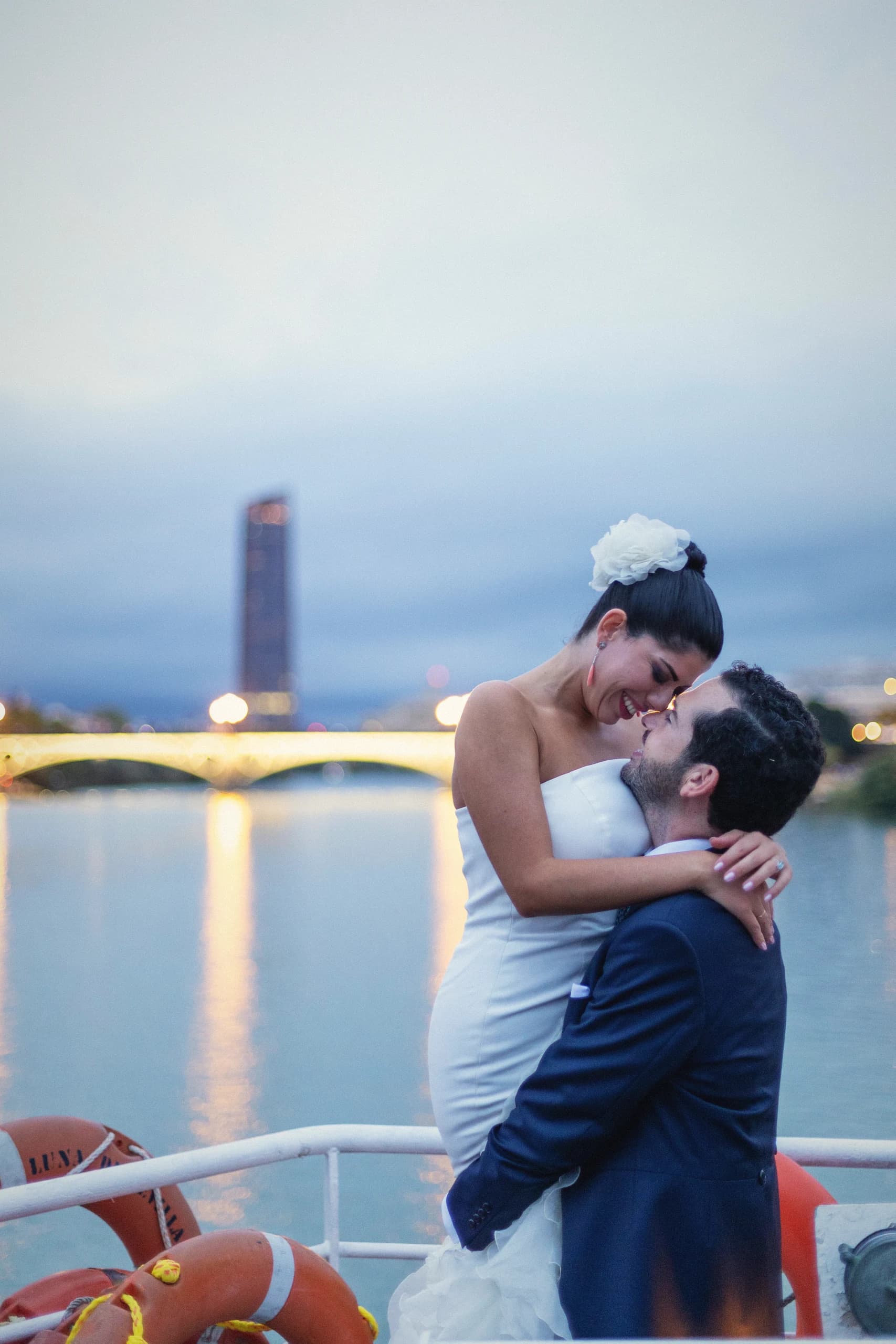 Beso en cubierta del barco al anochecer con el puente iluminado