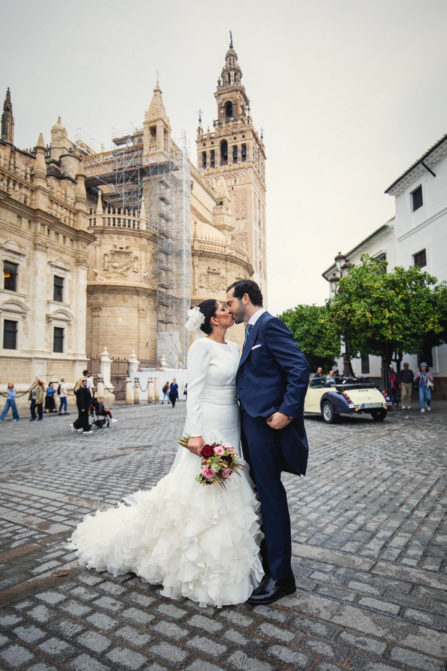 Los novios besándose junto al coche clásico con la Giralda al fondo