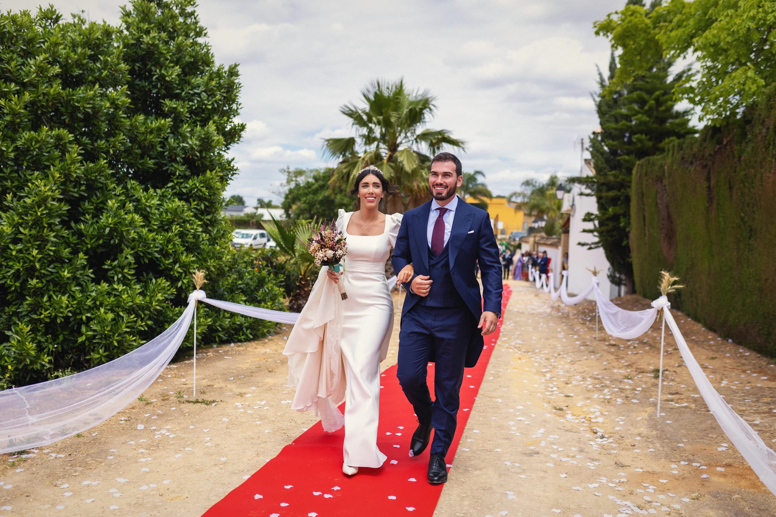 Los novios caminando por la alfombra roja entre los árboles de la hacienda