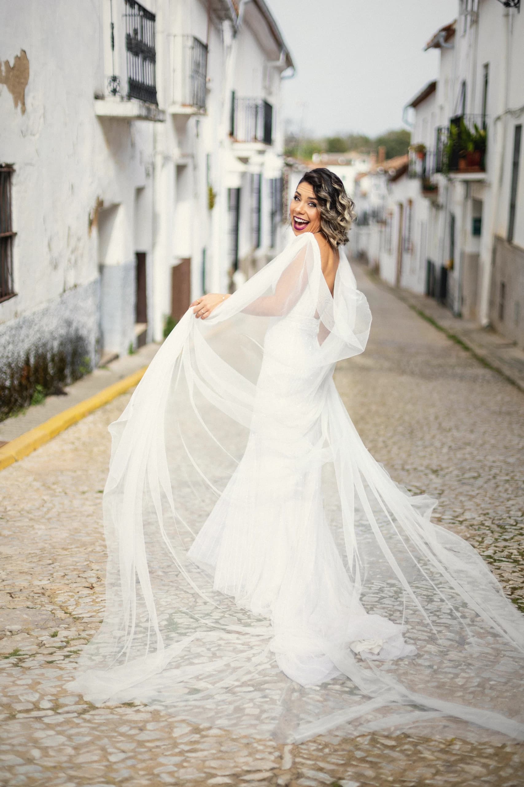 La novia haciendo volar el velo en una calle empedrada del pueblo