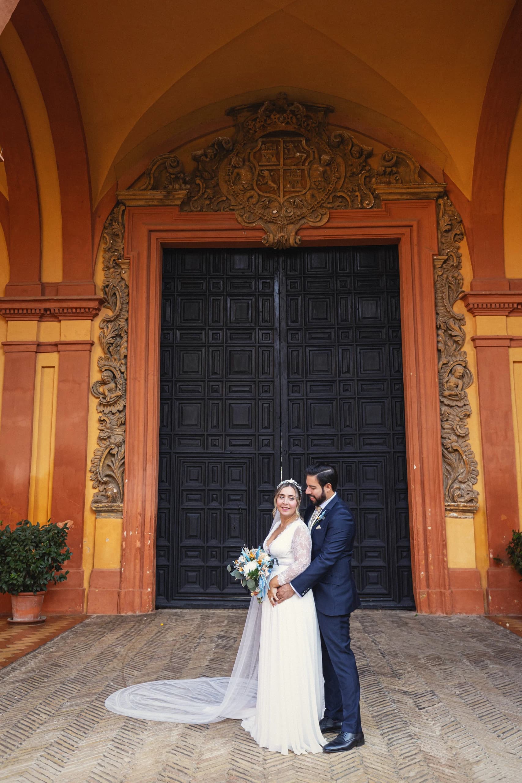 Los novios ante la gran puerta de madera del Alcázar, con la cola del vestido extendida