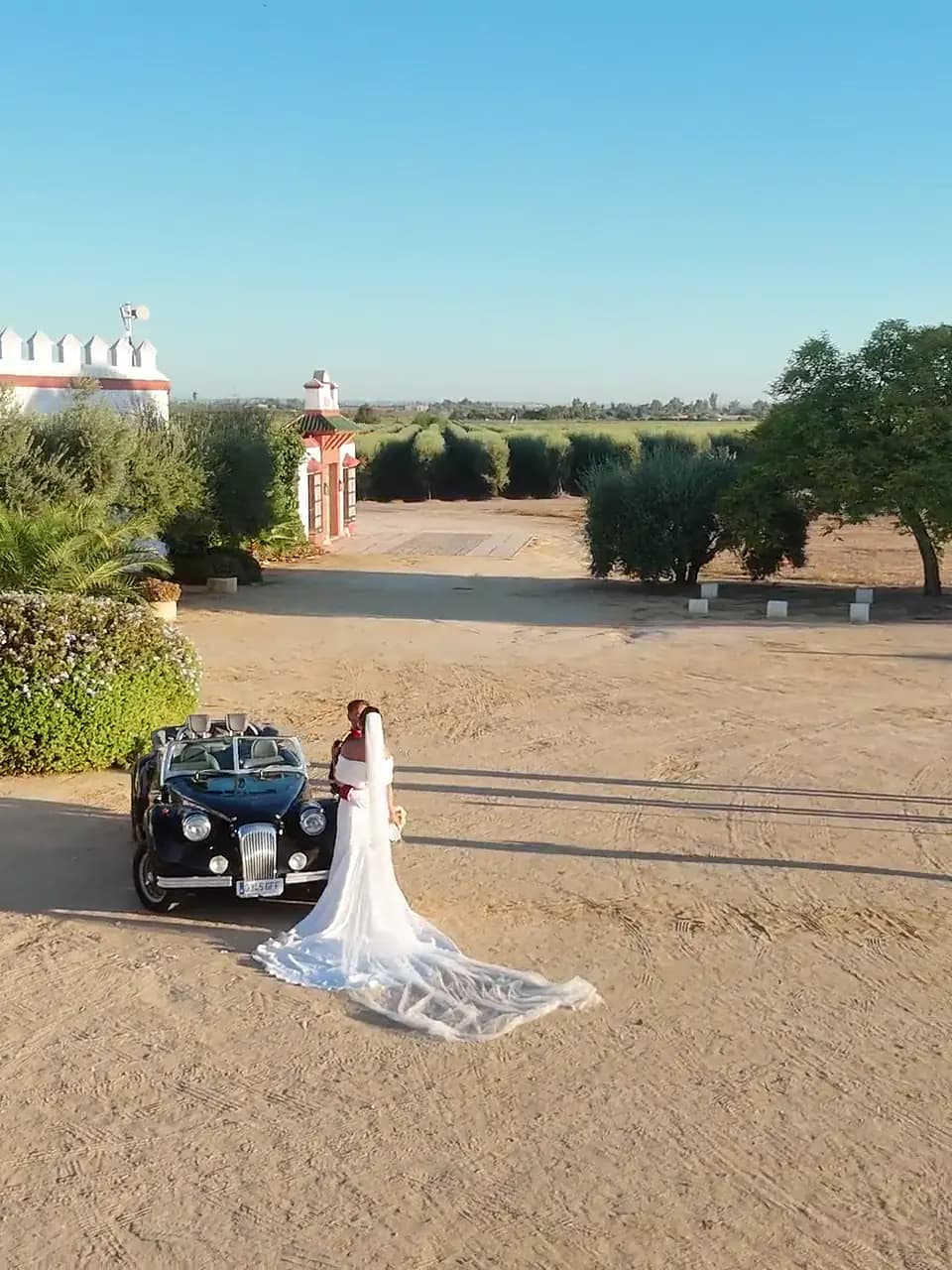 Los novios junto al coche clásico a las puertas de la hacienda, vistos desde el aire